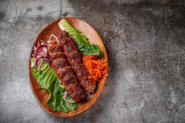 Serving a dish from the restaurant menu. Grilled beef and pork meat with grated carrots and herbs on a plate against a gray stone table, delicious kebab
