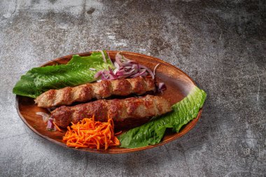 Serving a dish from the restaurant menu. Grilled beef and pork meat with grated carrots and herbs on a plate against a gray stone table, delicious kebab