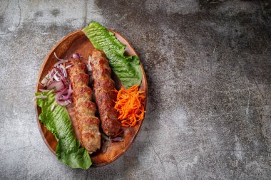 Serving a dish from the restaurant menu. Grilled beef and pork meat with grated carrots and herbs on a plate against a gray stone table, delicious kebab