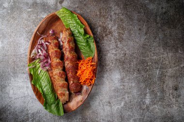 Serving a dish from the restaurant menu. Grilled beef and pork meat with grated carrots and herbs on a plate against a gray stone table, delicious kebab
