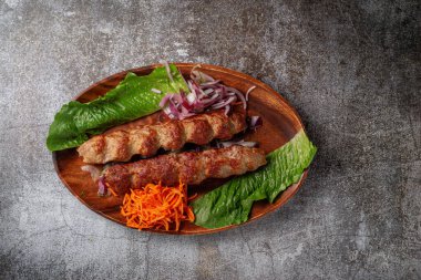 Serving a dish from the restaurant menu. Grilled beef and pork meat with grated carrots and herbs on a plate against a gray stone table, delicious kebab
