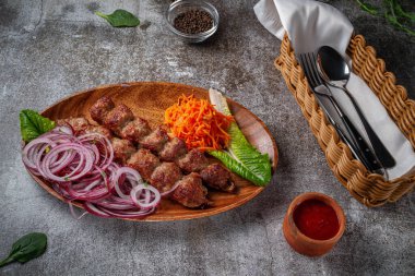 Meat kebab and barbecue with onions, Korean carrots and green salad in a plate against the background of a gray stone table 