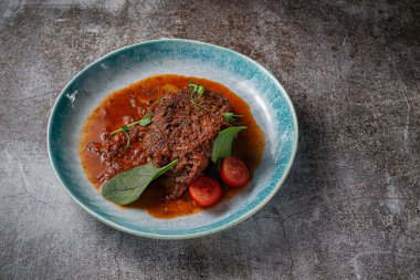 Beef stew with broth and herbs in a blue plate with spices and black pepper against a gray stone table
