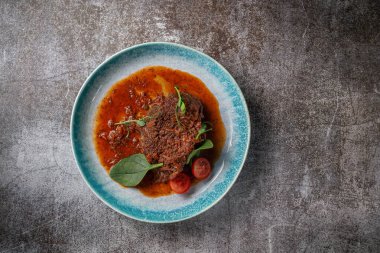 Beef stew with broth and herbs in a blue plate with spices and black pepper against a gray stone table