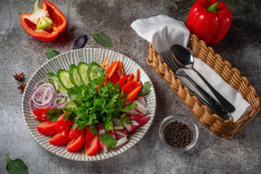 An appetizer in a restaurant, assorted vegetables. Sliced vegetables in layers on a plate with greens against a gray stone table