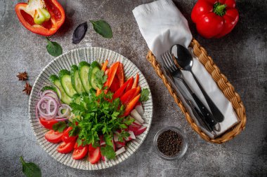 An appetizer in a restaurant, assorted vegetables. Sliced vegetables in layers on a plate with greens against a gray stone table