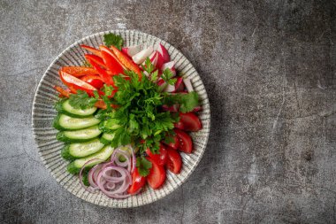 An appetizer in a restaurant, assorted vegetables. Sliced vegetables in layers on a plate with greens against a gray stone table