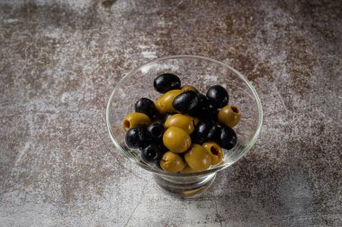 Olives and olives in a glass against the background of a gray stone tabl