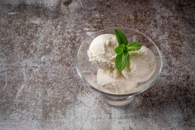 Balls of vanilla cream ice cream with mint in a glass against a backdrop of gray stone. Summer dessert. 