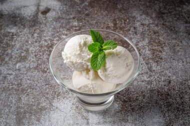 Balls of vanilla cream ice cream with mint in a glass against a backdrop of gray stone. Summer dessert. 