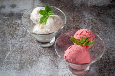 Pink and creamy strawberry mint cream ice cream balls in a glass beaker on a gray stone 