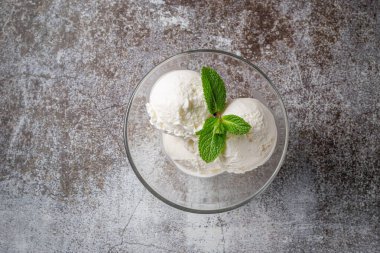 Balls of vanilla cream ice cream with mint in a glass against a backdrop of gray stone. Summer dessert. 