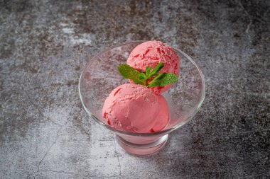 Pink balls of strawberry cream ice cream in a glass glass on a gray stone 