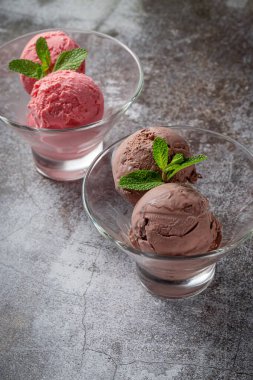 Pink strawberry and chocolate ice cream scoops in a cup against a gray stone table 