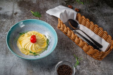 Mashed potatoes with fresh tomatoes on a blue plate against a gray stone table. A traditional, classic country dish