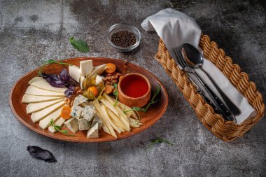 An appetizer in a restaurant, a cheese assortment. Sliced cheese in layers on a plate with greens against a gray stone table