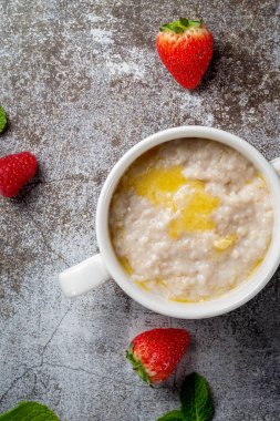 Oatmeal with butter and fresh raspberries and strawberries with mint in a white cup against a gray stone table. A healthy breakfast in a restaurant 
