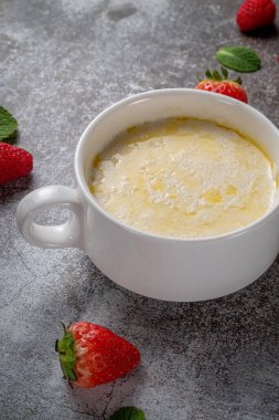 Cream of wheat, semolina pudding with butter and fresh raspberries and strawberries with mint in a white cup against a gray stone table. A healthy breakfast in a restaurant 