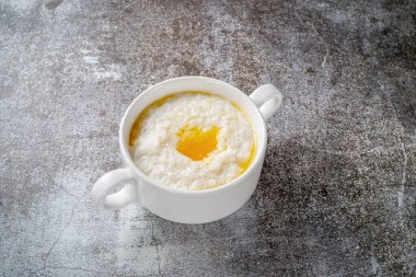 Rice porridge with butter in a white cup against a gray stone table. A healthy breakfast in a restaurant