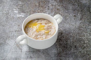 Oatmeal in a white cup against a gray stone table. A healthy breakfast in a restaurant 