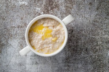 Oatmeal in a white cup against a gray stone table. A healthy breakfast in a restaurant 