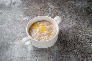 Oatmeal in a white cup against a gray stone table. A healthy breakfast in a restaurant 