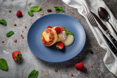 A delicious breakfast. Sweet fried pancakes with raspberries, strawberries and mint in a blue plate with sour cream on a gray stone table