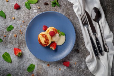 A delicious breakfast. Sweet fried pancakes with raspberries, strawberries and mint in a blue plate with sour cream on a gray stone table
