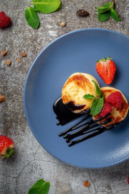 Fried pancakes with chocolate syrup and raspberries and mint in a blue plate against a gray stone table. A sweet breakfast in the morning 