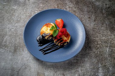 Fried pancakes with chocolate syrup and raspberries and mint in a blue plate against a gray stone table. A sweet breakfast in the morning 