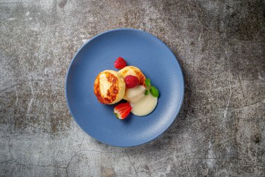 A delicious breakfast. Sweet fried pancakes with raspberries, strawberries and mint in a blue plate with sour cream on a gray stone table