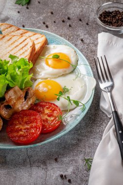 Serving a dish from the restaurant menu. Delicious and healthy breakfast with fried eggs, beans, sausages, grilled vegetables, tomatoes and mushrooms with salad on a plate against a gray stone table