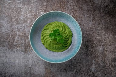 Green spinach and avocado cream soup in a blue plate with parsley and dill against a gray stone tabl