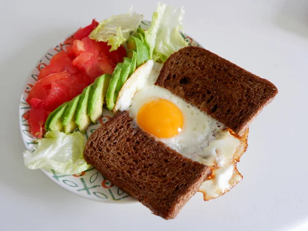 Full plate with home made breakfast food on white table. Healthy brunch with fried egg, two pieces of wholegrain dark bread, slices of avocado and tomatoes.