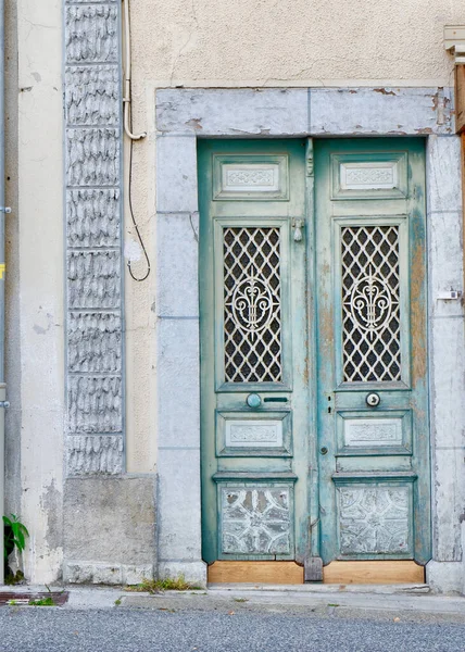 Vintage shabby door of light blue colour outside on the street of Arreau town, France.