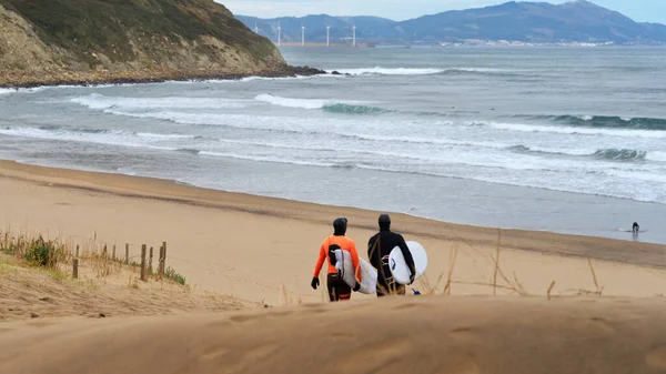 Image with people surfing walking along beach towards ocean.