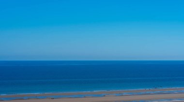 Beautiful panoramic view of ocean, natural beach, silhouettes of people and clear sky.