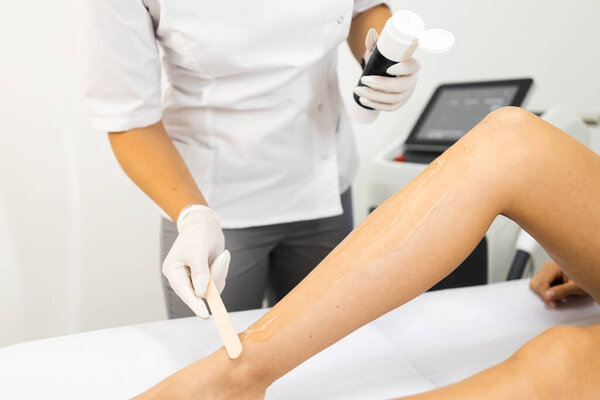 Beautician applies a special gel for laser hair removal to a woman's leg