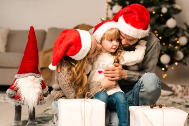 Aileler evde yerde otururken kızlarına sarılır ve ona Noel hediyeleri verir.