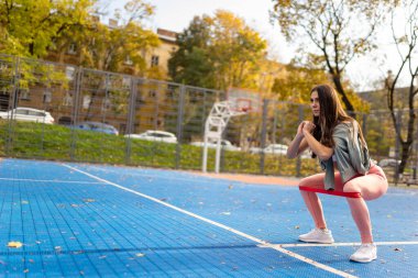Atletik kız direniş bantlarıyla çömeliyor.