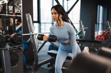 Kadın, dambıllarla egzersiz yaparken kaslarını sallıyor.