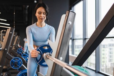 Spor yaparken halterin üzerine metal disk takan atletik bir kadın.