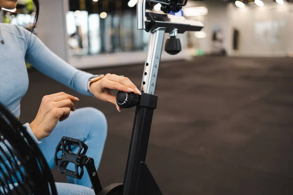 Spor salonundaki kadın egzersiz bisikletindeki koltuğu ayarlıyor.