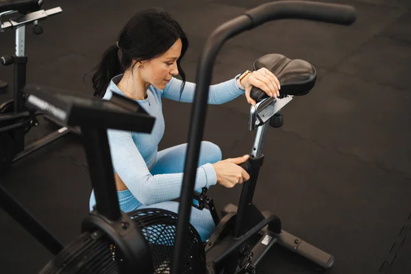 Güzel bir fitness kadını egzersiz yapmadan önce bisiklet koltuğunun yüksekliğini ayarlar.