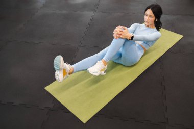 Karın kası egzersizi yapan kadın sporcu yoga minderinde mekik çekiyor.