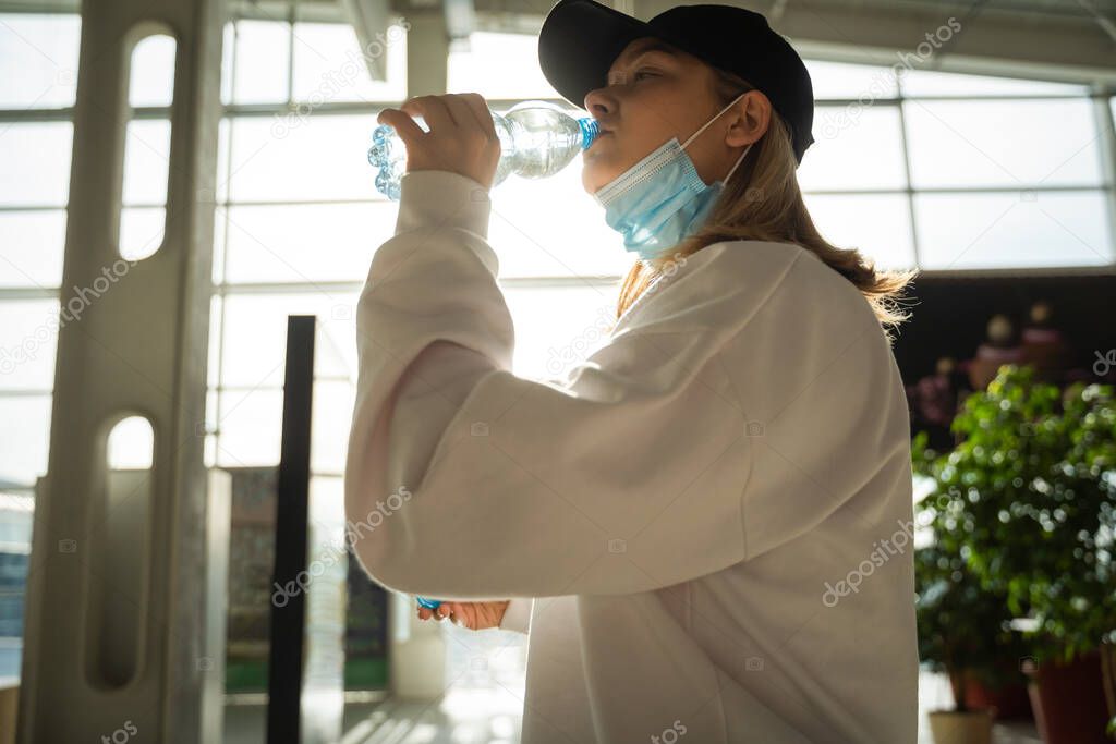 Young girl with a medical mask drinks water from a bottle