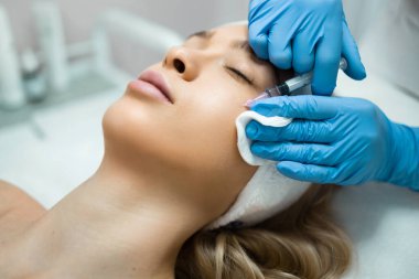 Woman getting cosmetic injection of botox in cheek. Anti-aging procedure and face lift in cosmetology clinic