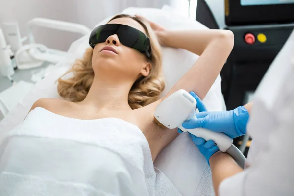 Pretty woman having underarm laser hair removal procedure in beauty salon. Skin care.