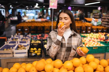 Woman smell orange while shopping in grocery supermarket