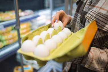Close up of female hands choosing eggs in a supermarket. Woman buys eggs. Girl holding a package of eggs in her hands